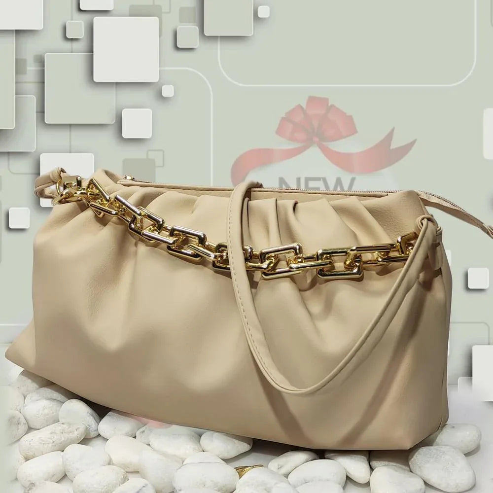 Beige handbag with gold chain handle on a textured surface