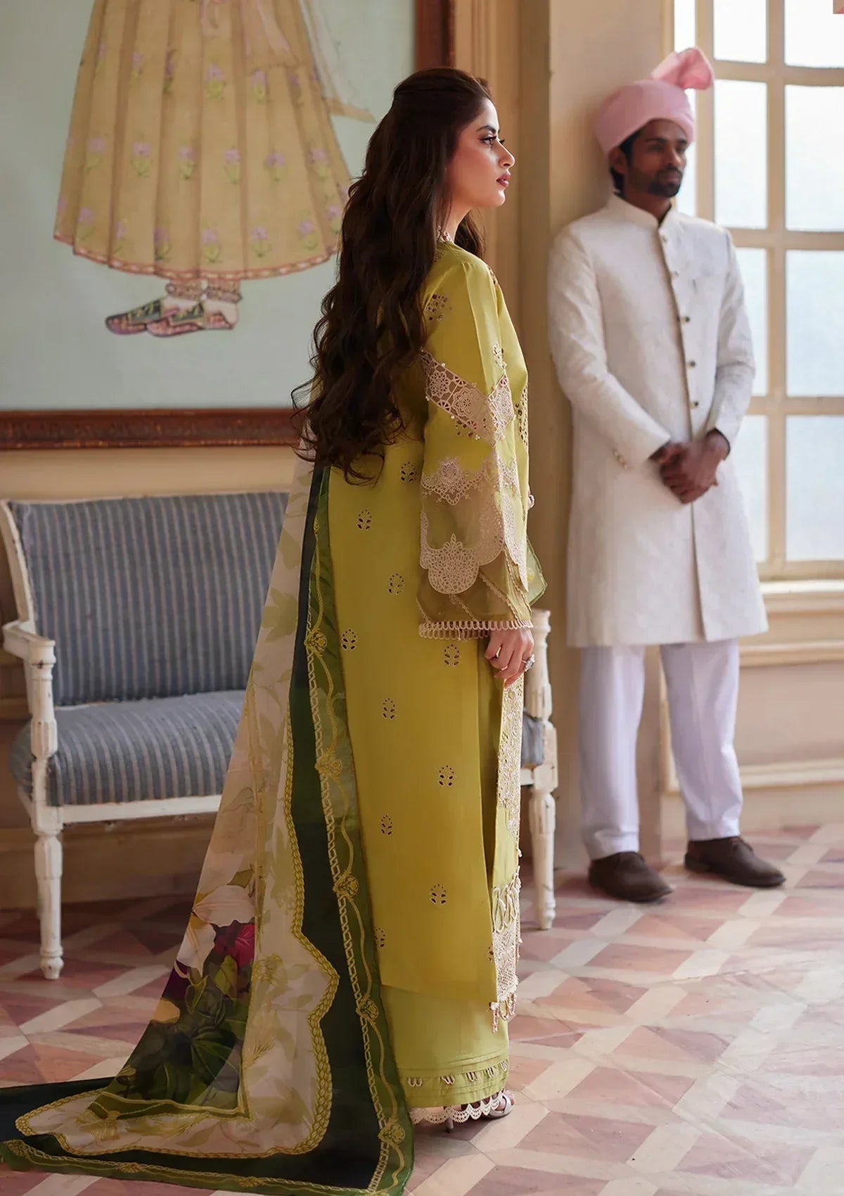 Woman in a yellow and green traditional outfit standing in a room with a man in a white suit and pink turban.