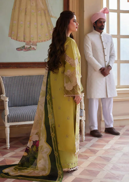 Woman in a yellow and green traditional outfit standing in a room with a man in a white suit and pink turban.
