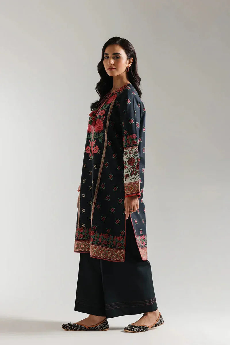 Woman wearing a long, patterned coat over a black outfit on a plain background