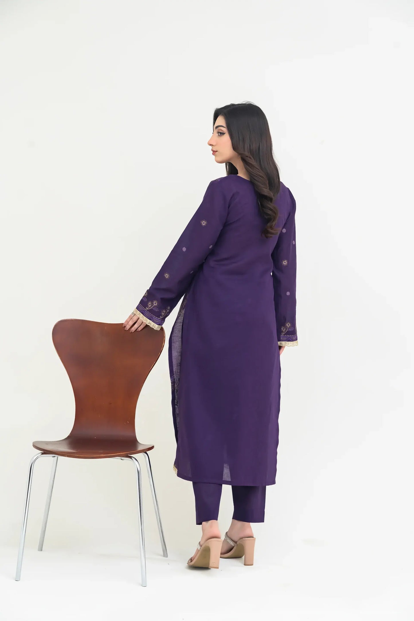 Woman in a purple outfit standing next to a brown chair on a white background
