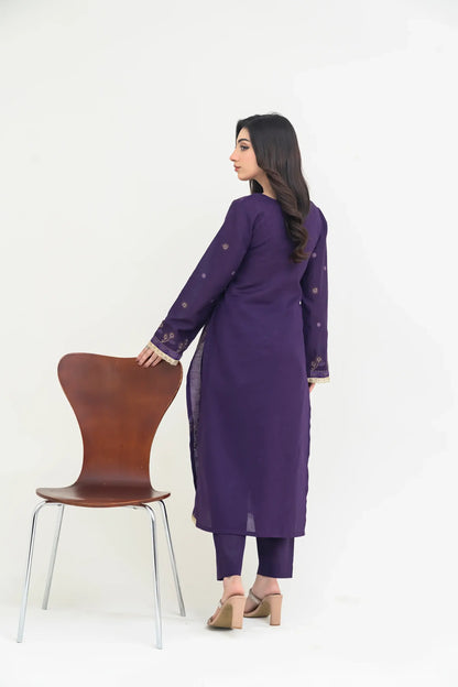 Woman in a purple outfit standing next to a brown chair on a white background