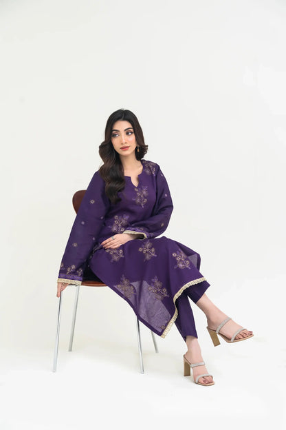 Woman wearing a purple traditional outfit with floral patterns, sitting on a chair against a white background.