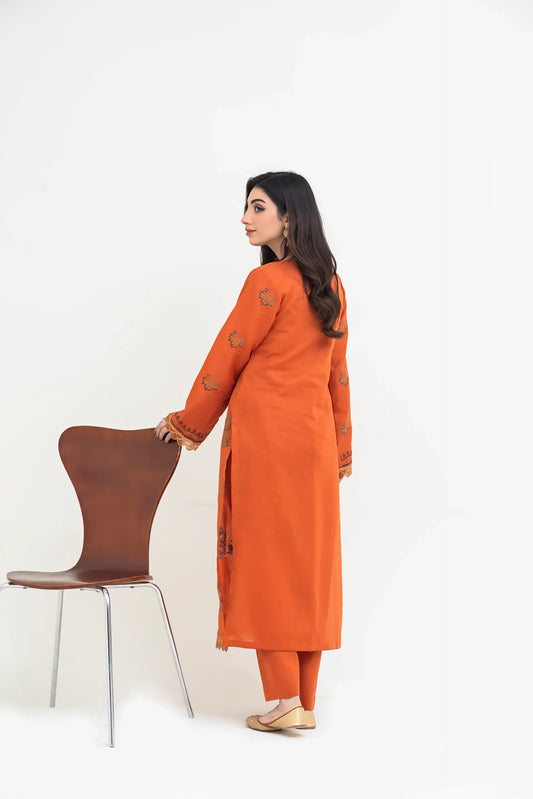 Woman in an orange traditional outfit standing next to a brown chair on a white background