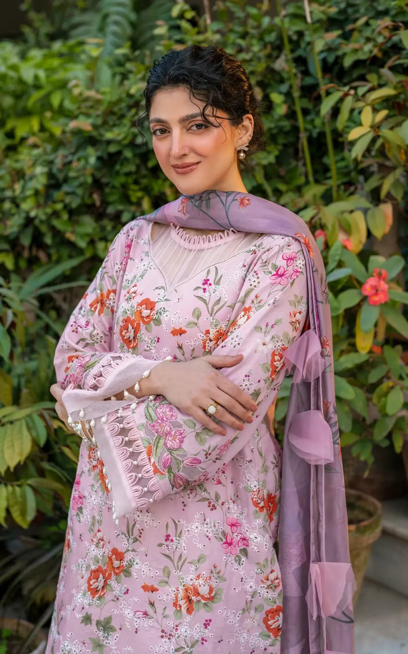 Woman wearing a pink floral saree with a green leafy background