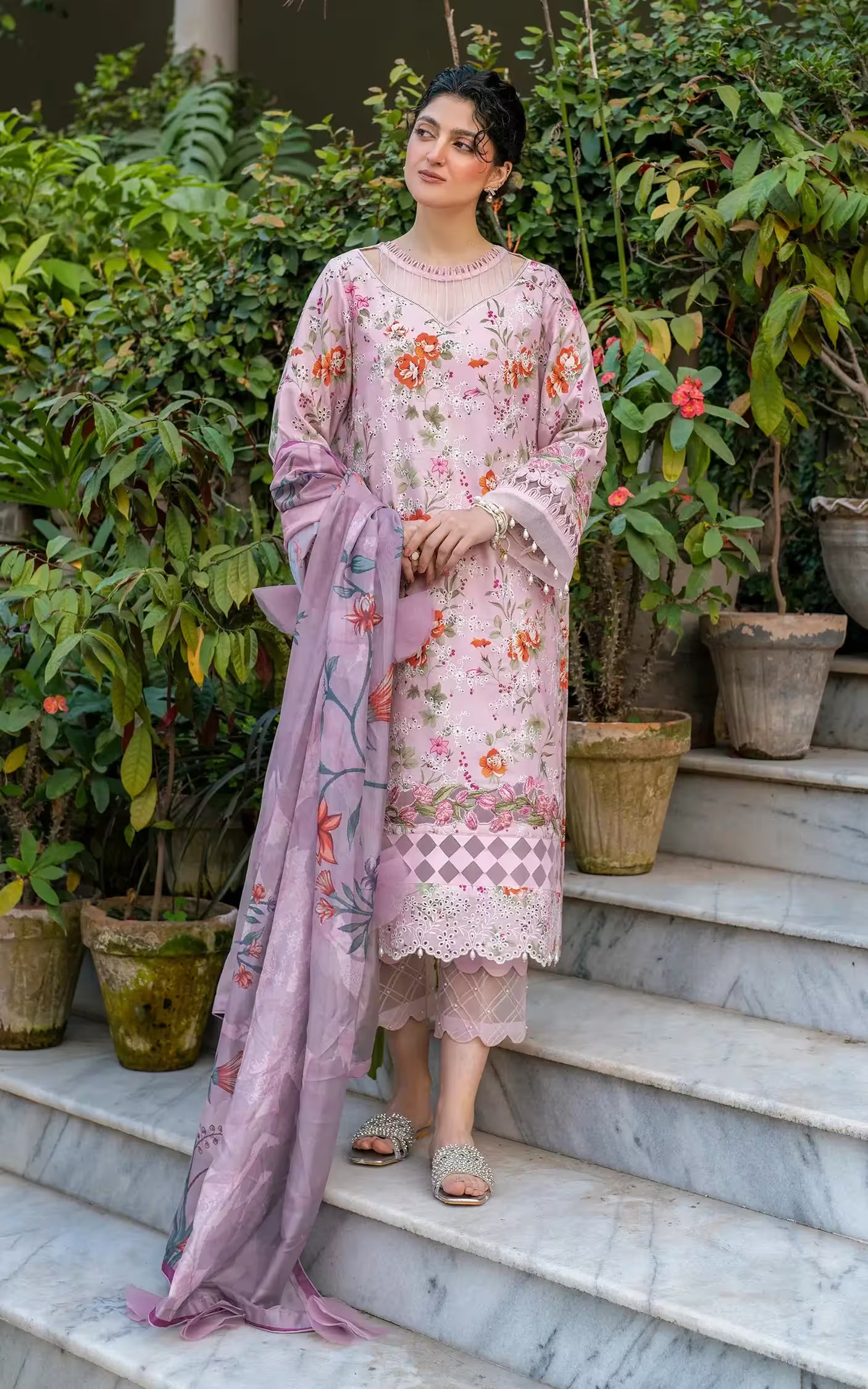 Woman in a pink floral dress standing on steps with greenery around