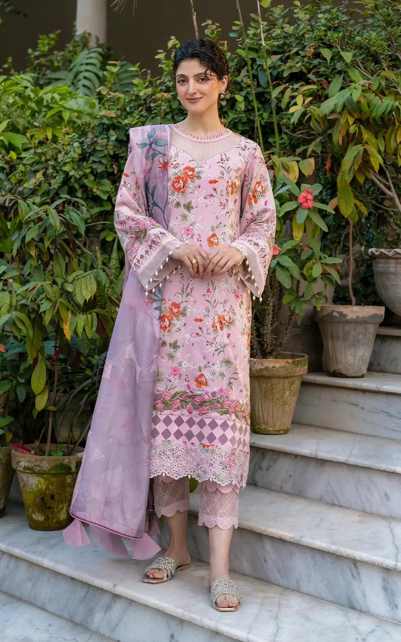 Woman in a pink floral outfit standing on steps with greenery in the background