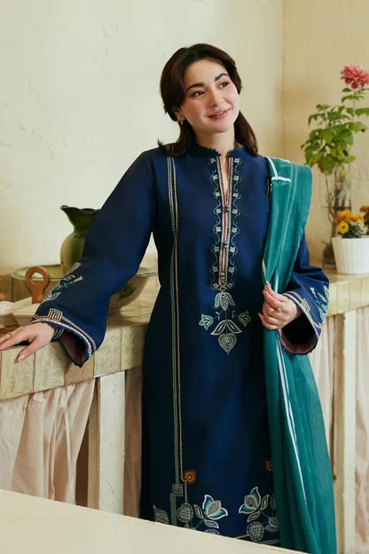 Woman wearing a blue embroidered dress with a green dupatta in an indoor setting.