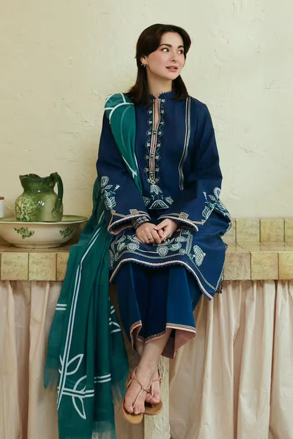 Woman in a blue and green traditional outfit sitting on a ledge with a decorative background.