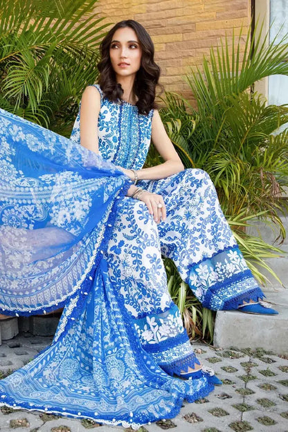 Woman in a blue and white embroidered saree sitting outdoors with plants in the background