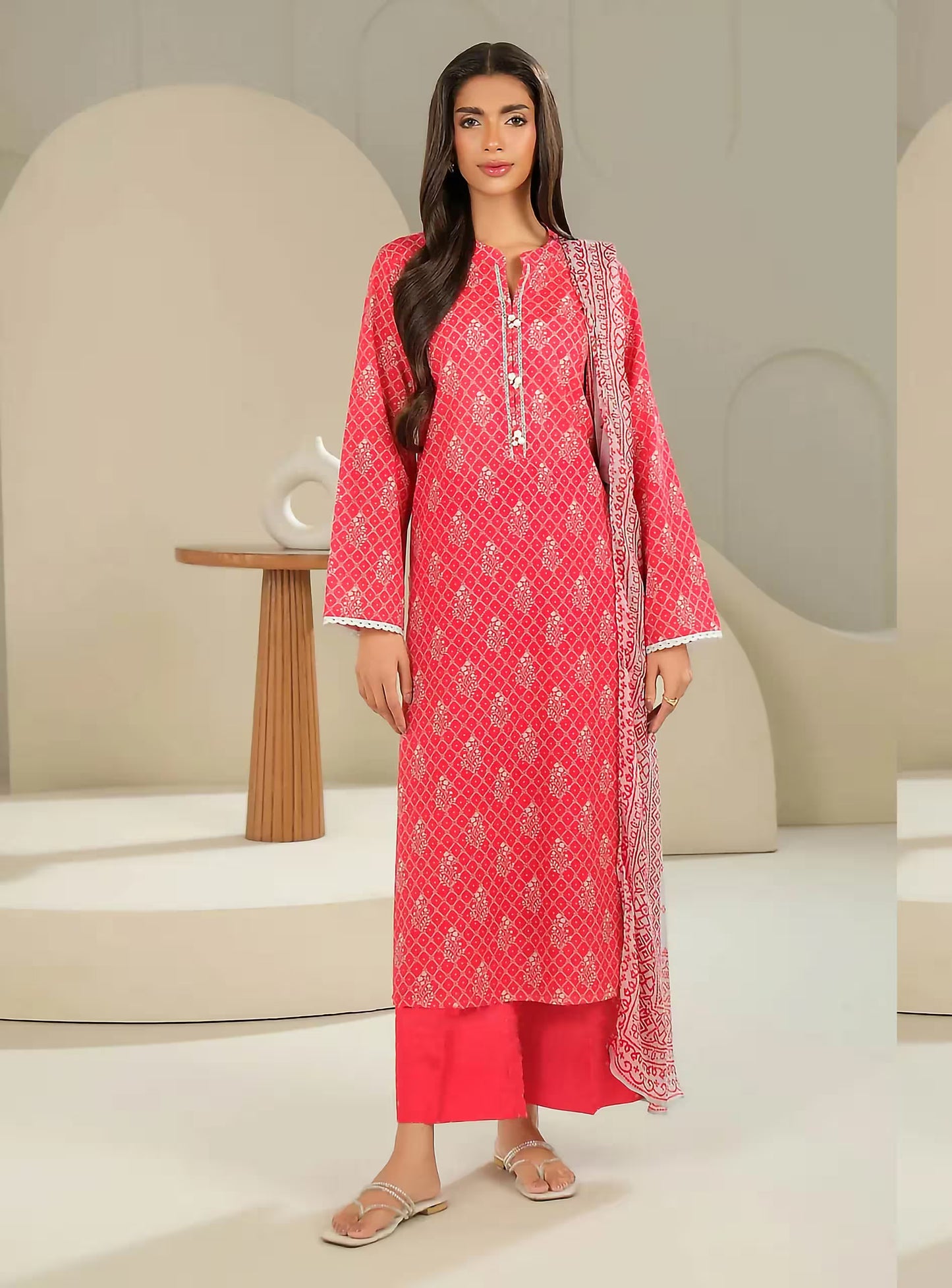 Woman wearing a red patterned outfit with a matching dupatta in a minimalistic setting.