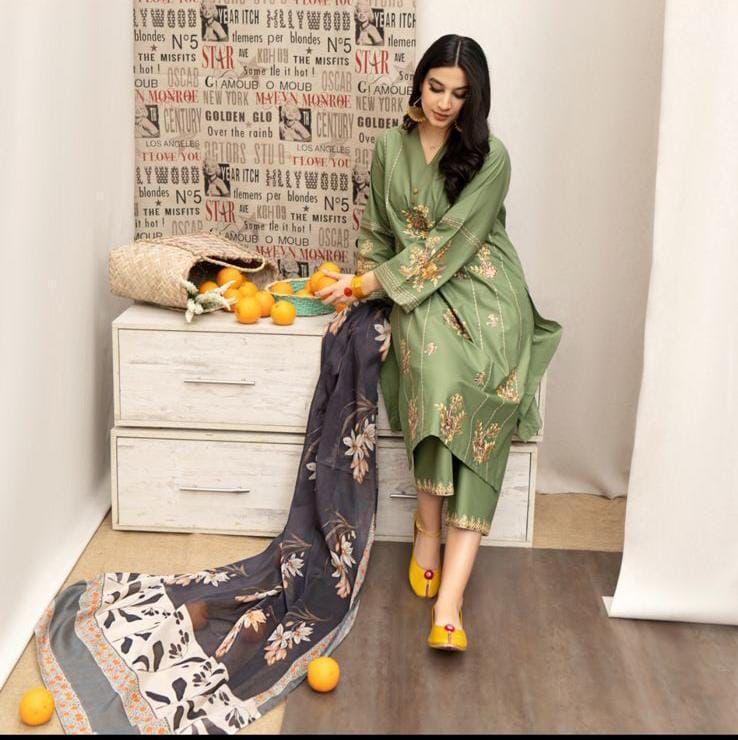 Woman in a green traditional outfit sitting on a white dresser with a patterned wall behind her.