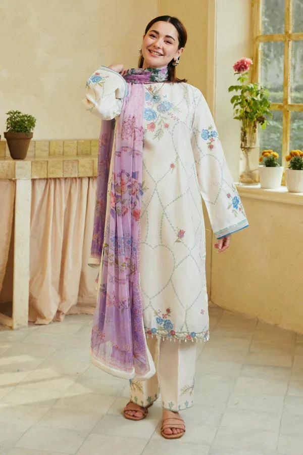 Woman in a white embroidered outfit with a purple scarf in a room with a window and plants.