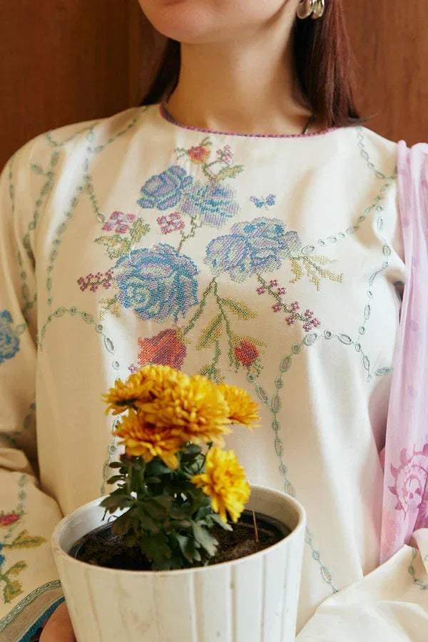 Person wearing a floral embroidered outfit holding a potted plant with yellow flowers.