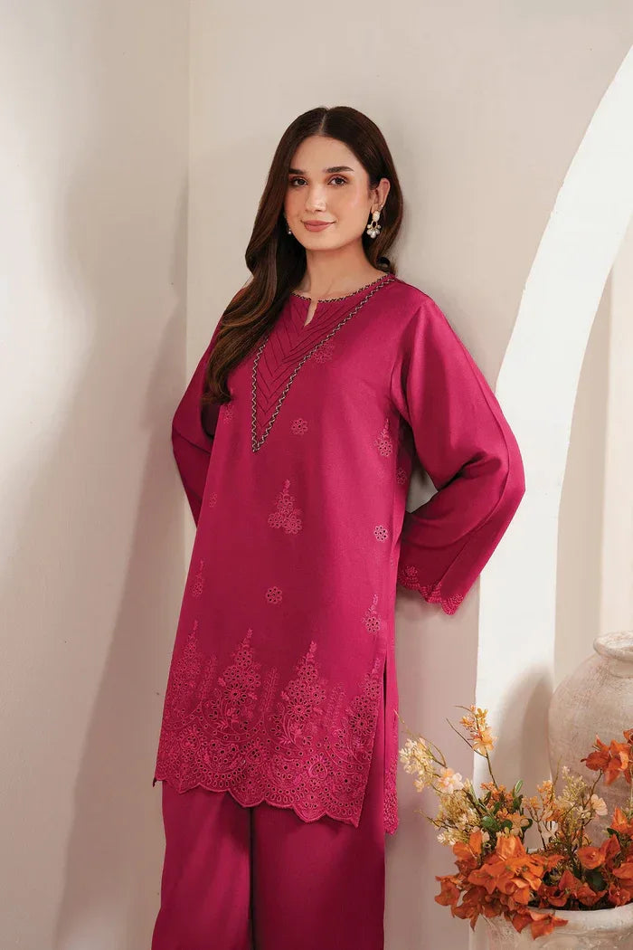 Woman wearing a pink traditional outfit with floral embroidery in a softly lit room.