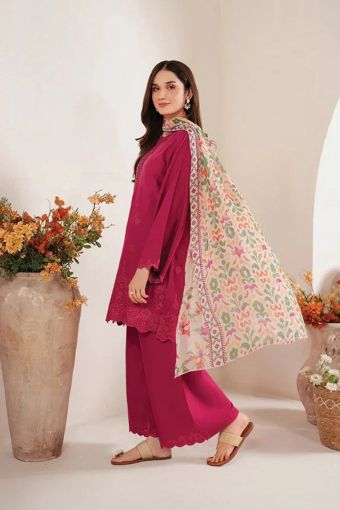 Woman in a magenta traditional outfit with a floral dupatta, standing indoors with decorative plants.