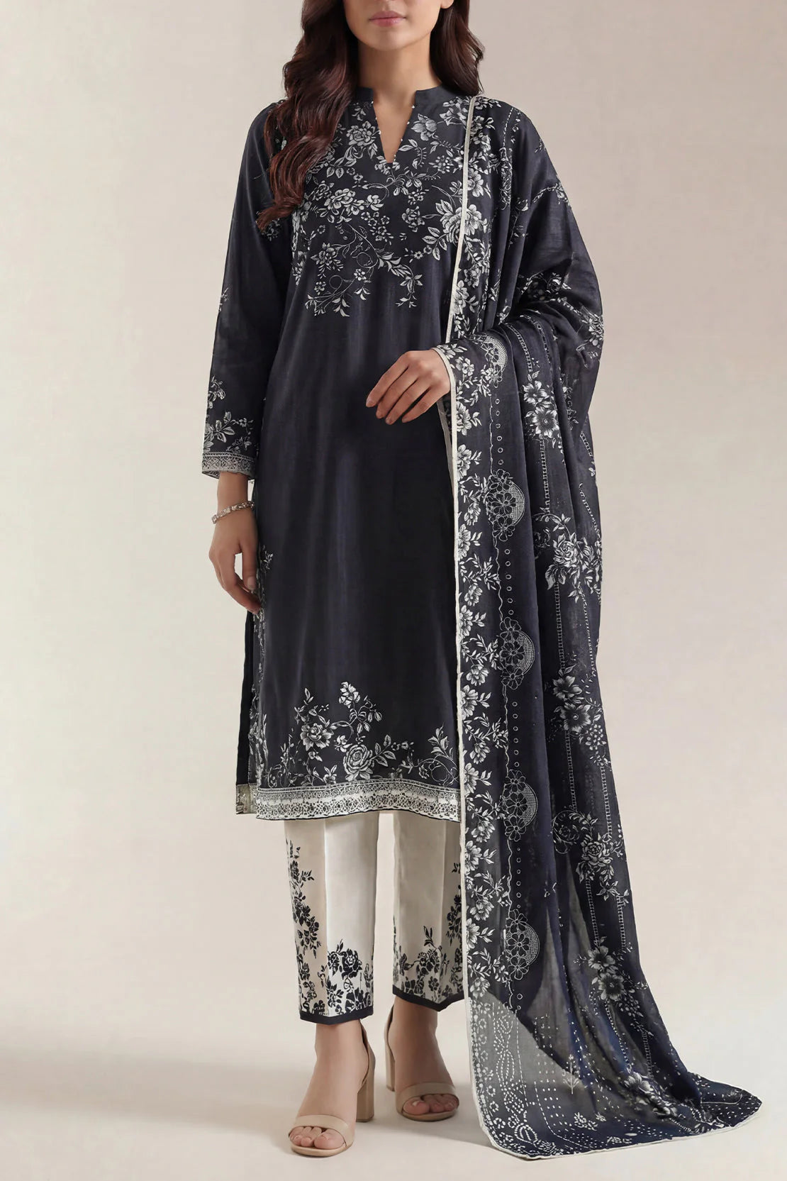 Woman wearing a dark blue embroidered outfit with white pants and matching dupatta on a plain background