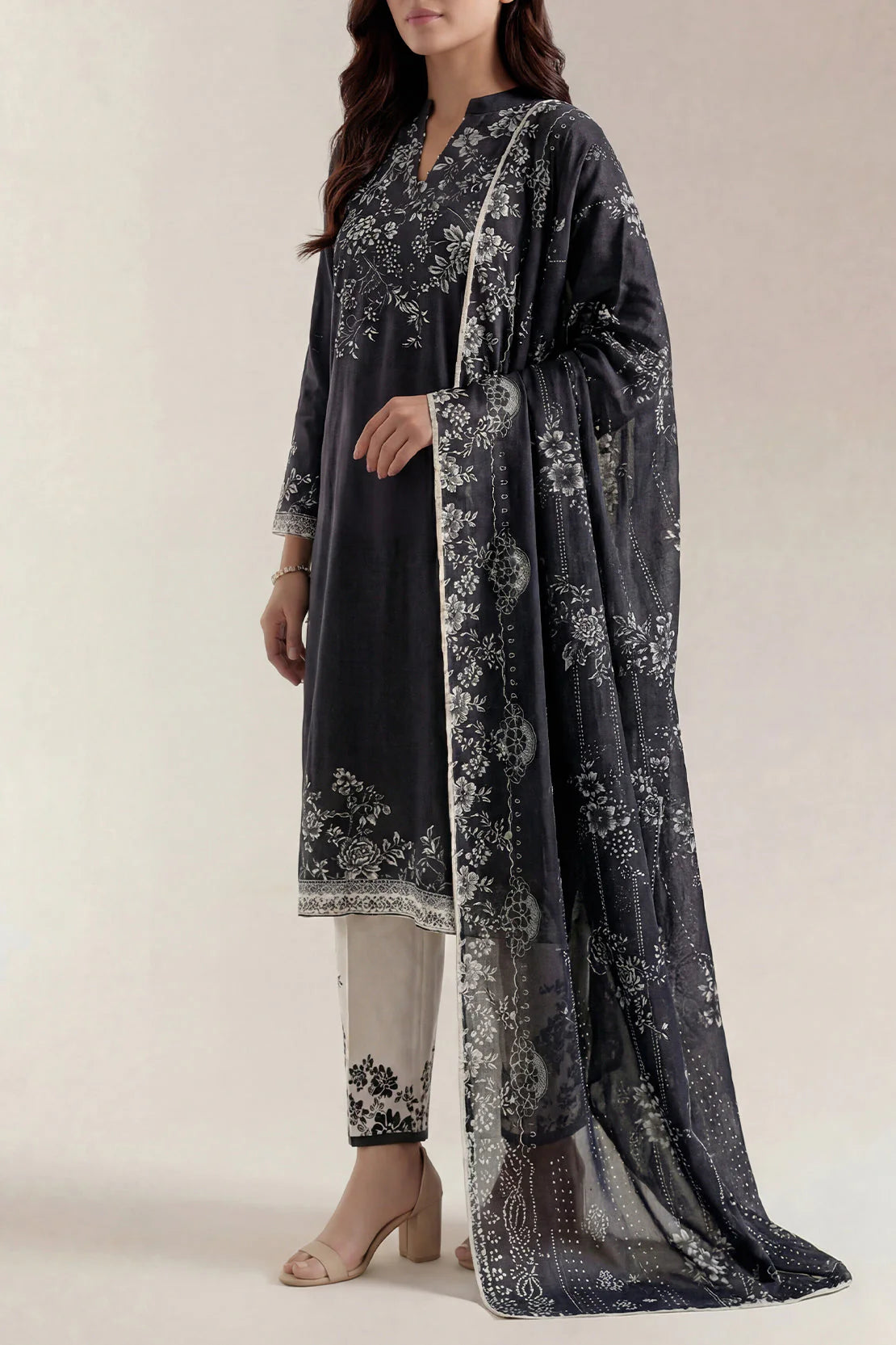 Woman wearing a dark gray floral printed outfit with a matching dupatta on a light background