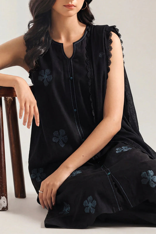 Woman wearing a black sleeveless top with floral embroidery sitting on a chair.