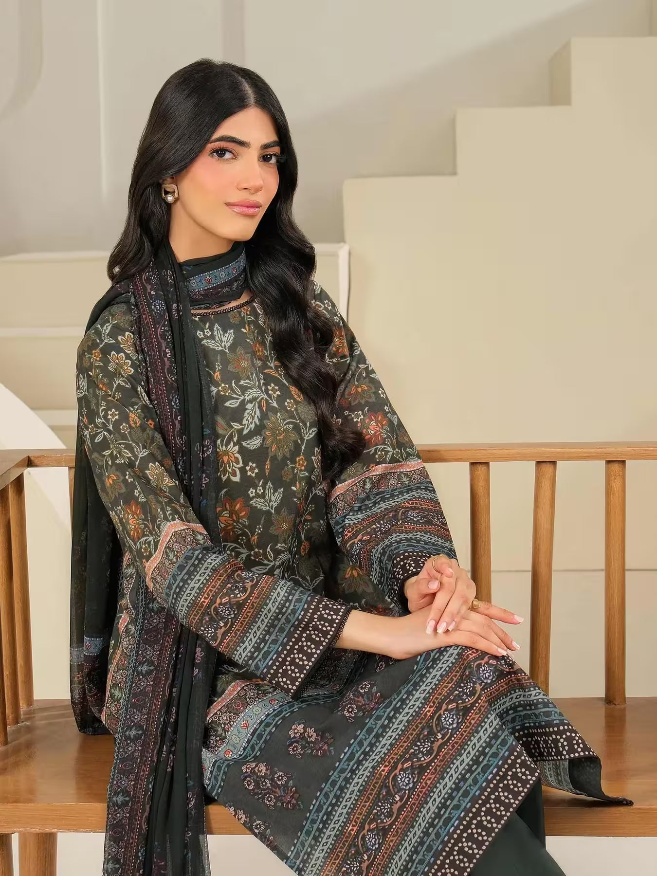 Woman wearing a patterned outfit sitting on a wooden chair indoors.