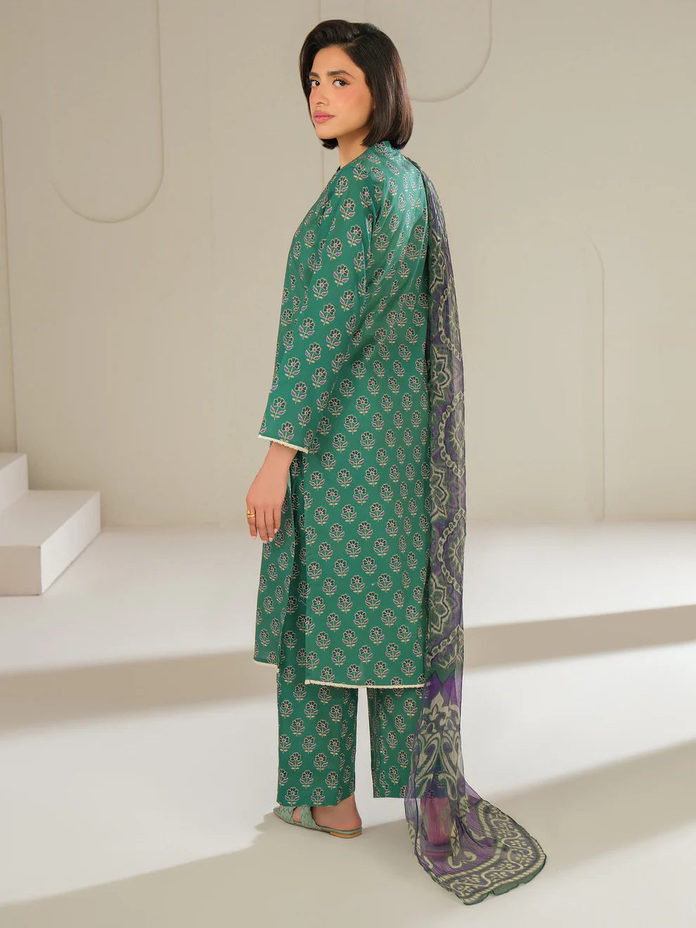 Woman wearing a green traditional outfit with a matching dupatta in a minimalistic setting