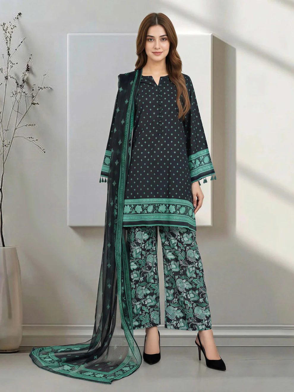 Woman wearing a black and green traditional outfit with a long scarf in a minimalistic room.