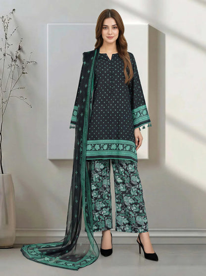 Woman wearing a black and green traditional outfit with a long scarf in a minimalistic room.