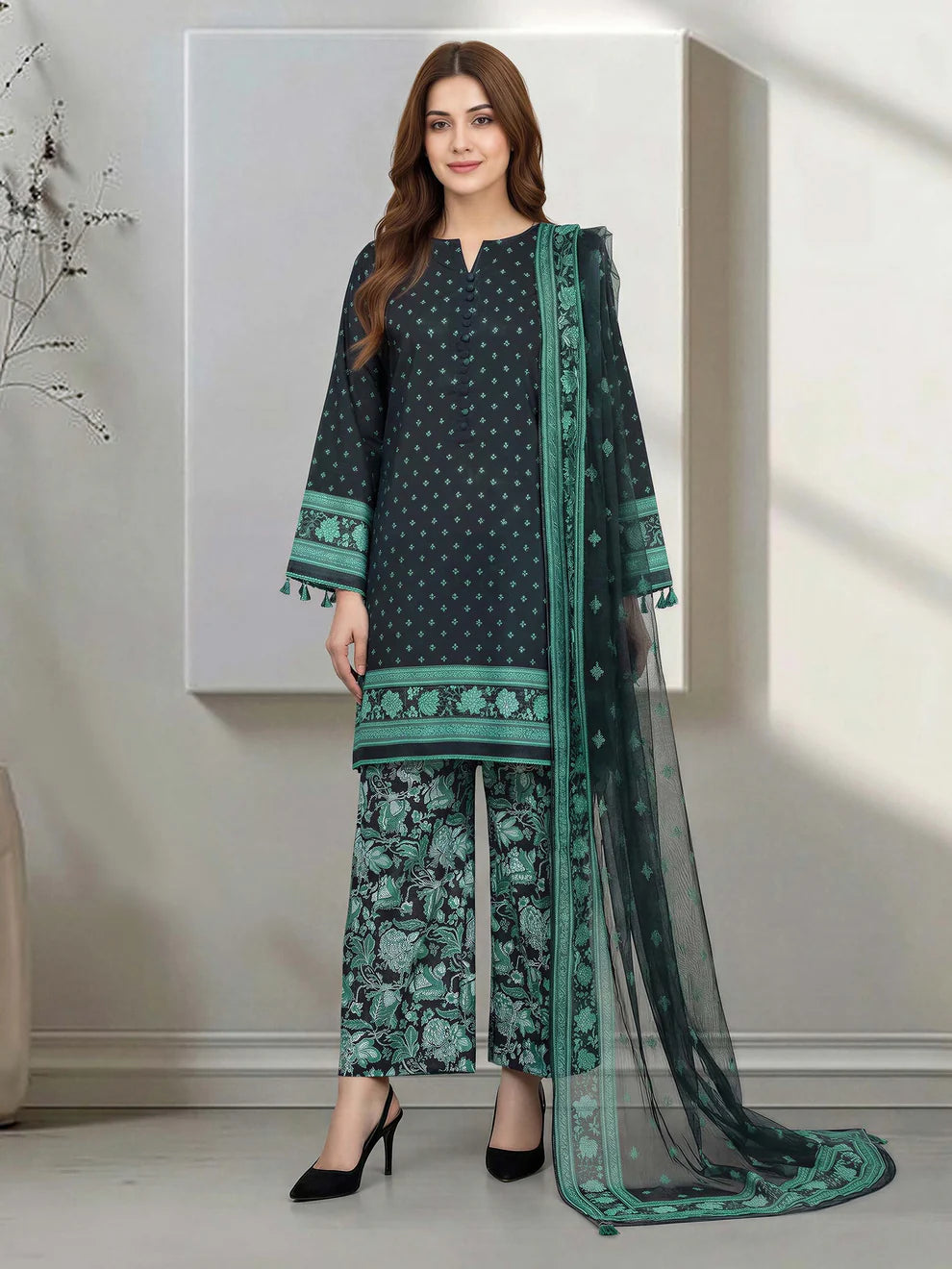 Woman wearing a green and black traditional outfit with a dupatta in a minimalistic room.