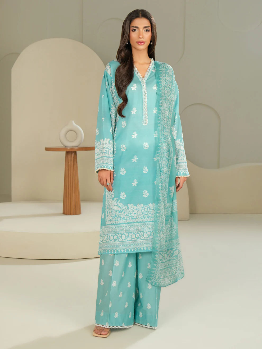Woman wearing a light blue embroidered traditional outfit in a minimalistic setting