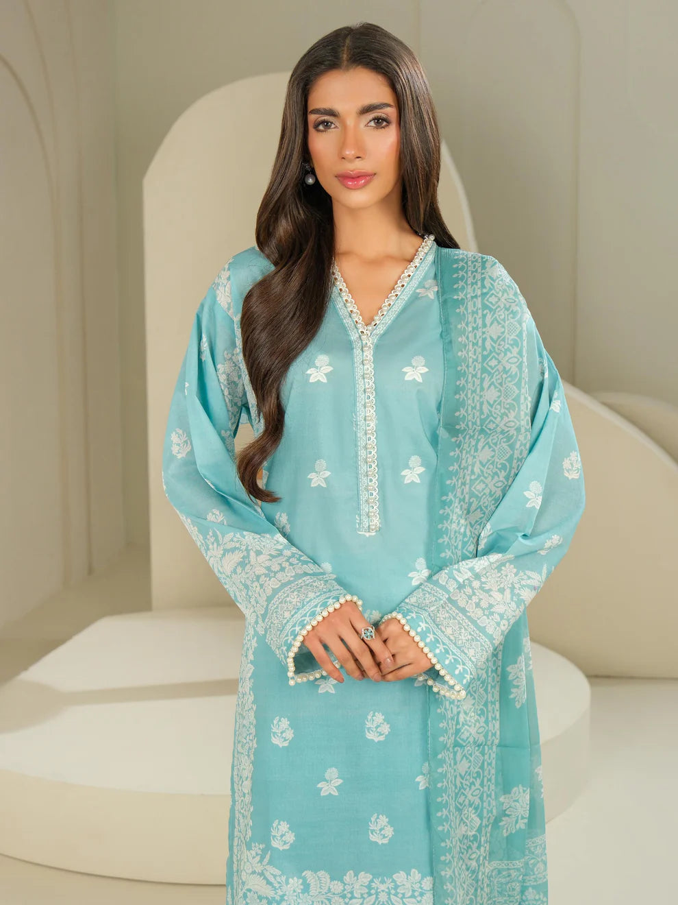 Woman wearing a light blue embroidered dress sitting on a white chair.