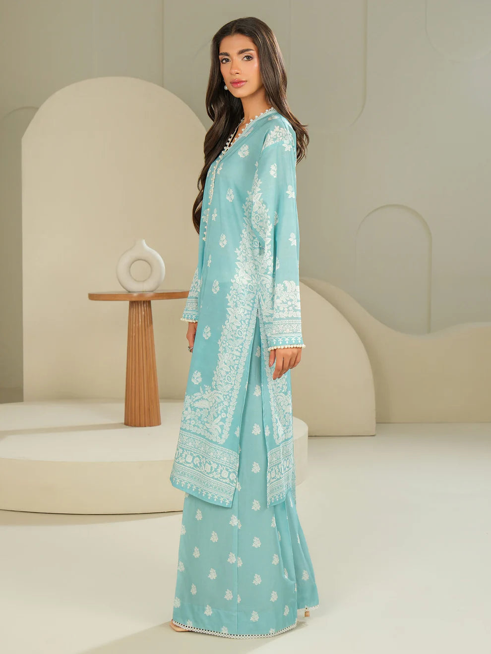 Woman wearing a light blue embroidered traditional outfit in a minimalistic setting