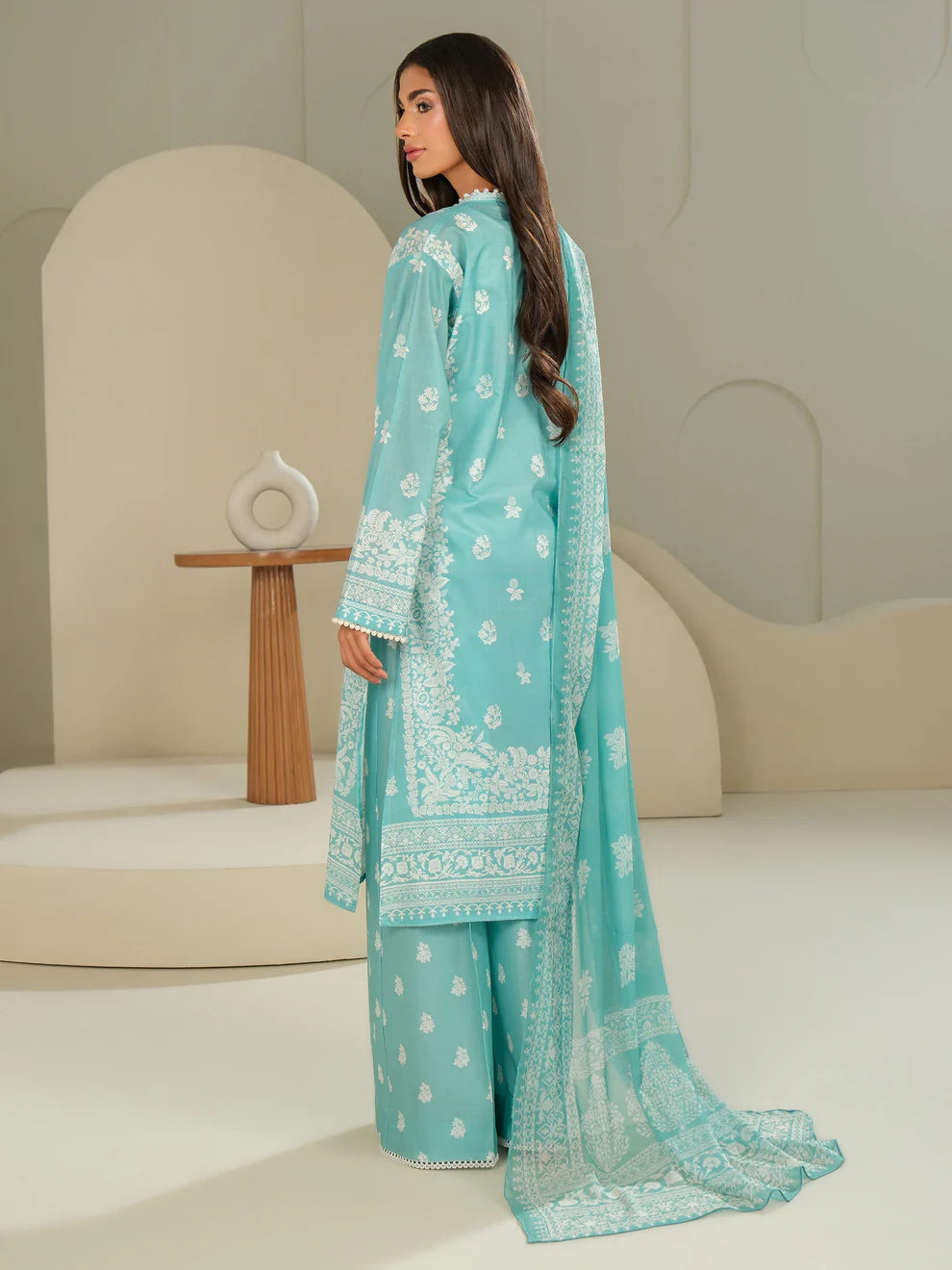 Woman wearing a light blue embroidered traditional outfit in a minimalistic setting