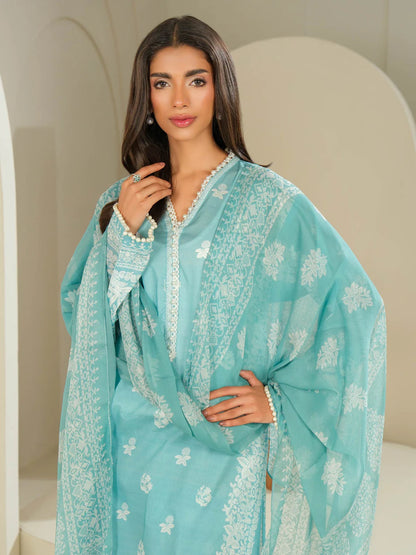 Woman wearing a light blue traditional outfit with white patterns indoors.