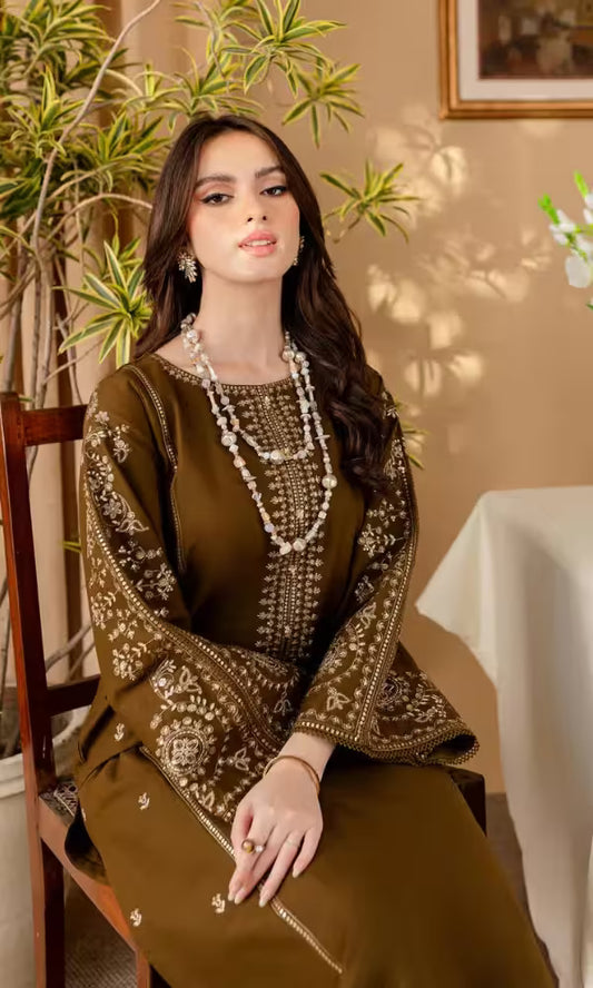 Woman in an embroidered brown outfit sitting in a decorated room with plants and a tablecloth.
