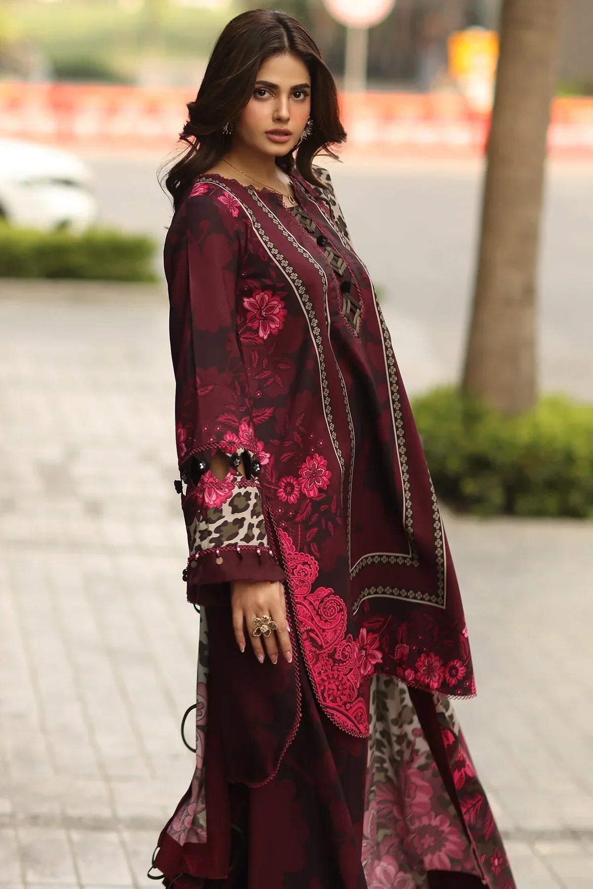 Woman wearing a maroon embroidered traditional outfit with a blurred outdoor background