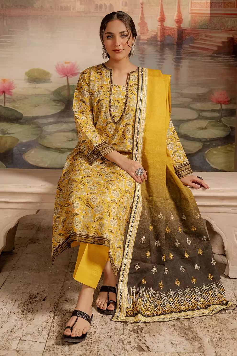 Woman in a yellow and brown traditional outfit sitting on a stone bench with a scenic background.