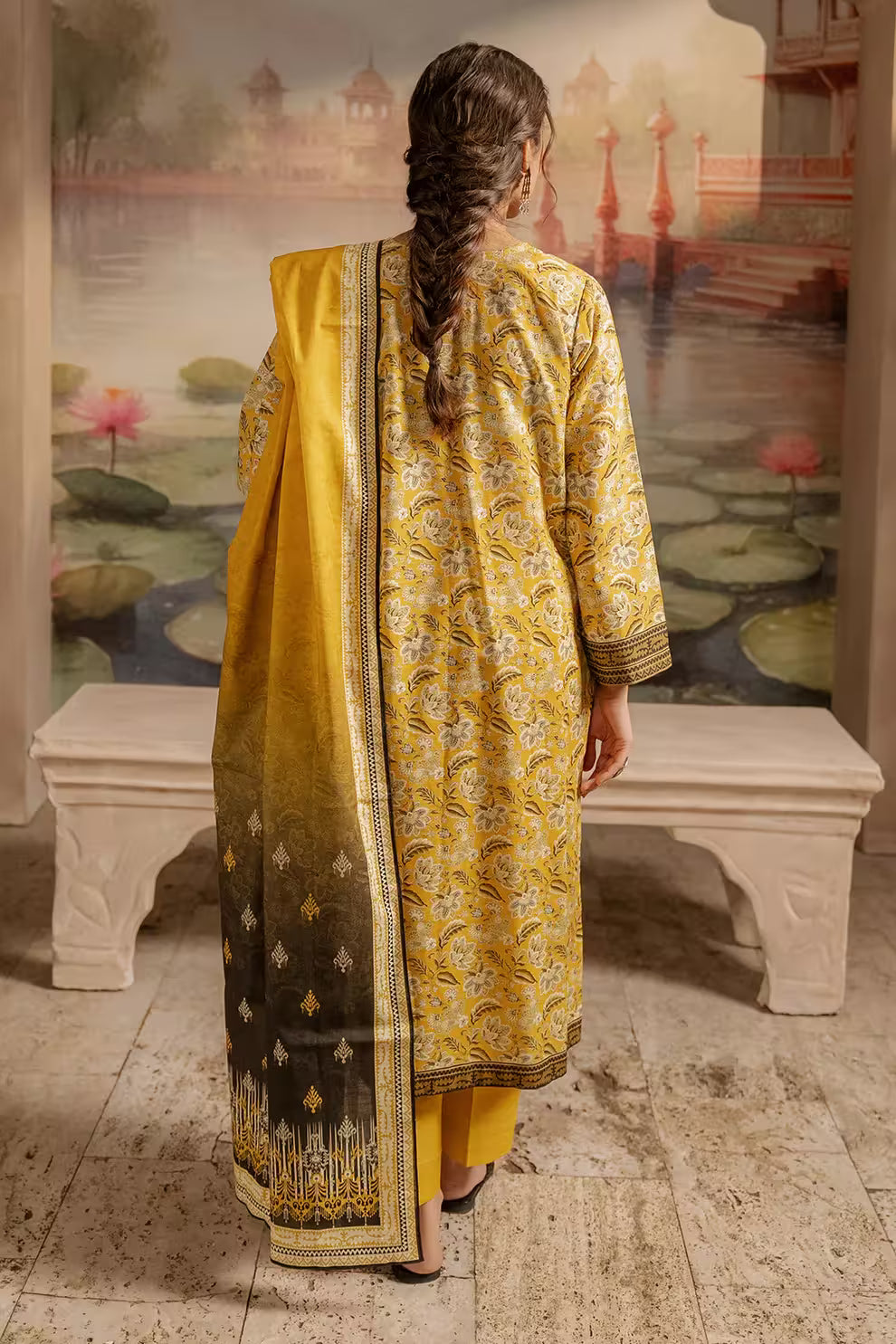 Woman in a yellow and black patterned outfit standing in front of a scenic mural.