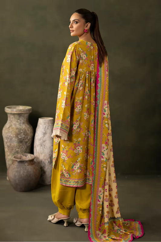 Woman in a yellow traditional outfit with a floral dupatta, standing against a dark background.