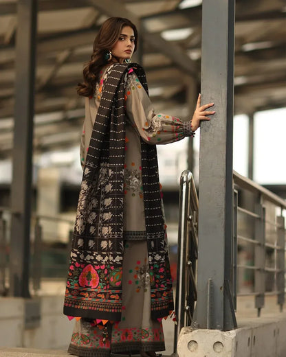 Woman in traditional embroidered outfit standing against a metallic structure.