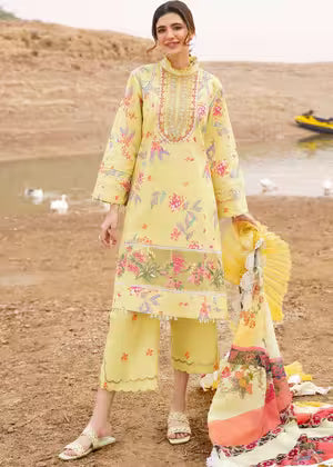 Woman in a yellow embroidered outfit standing in a desert-like setting with water and boats in the background.
