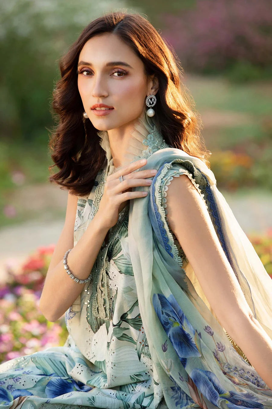 Woman in a floral dress with a scarf, standing outdoors with flowers in the background
