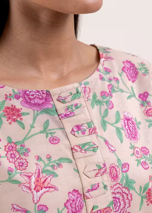 Close-up of a person wearing a floral-patterned shirt with pink and green flowers on a light background.