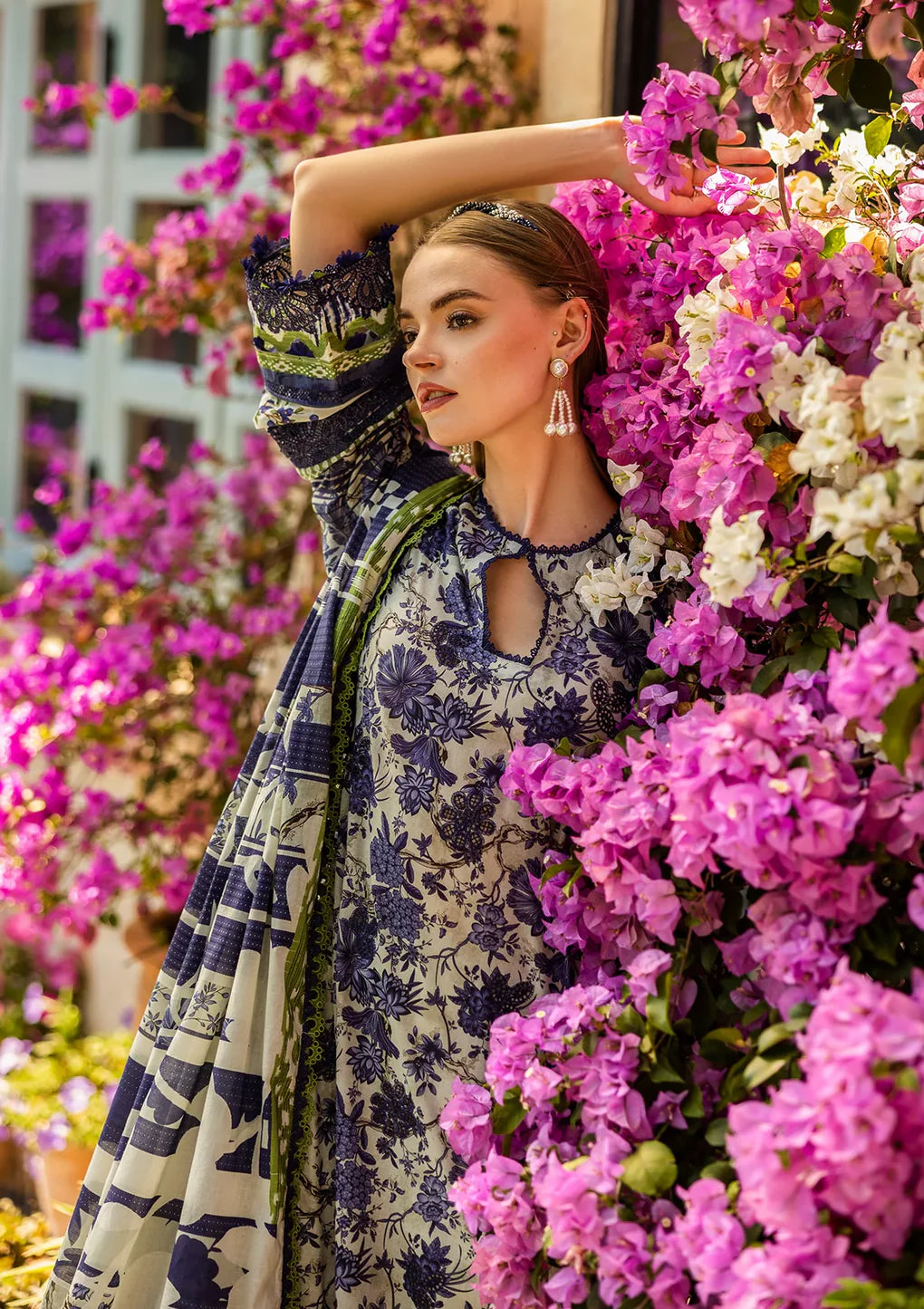 Woman in a floral dress standing among pink flowers with a blurred building in the background