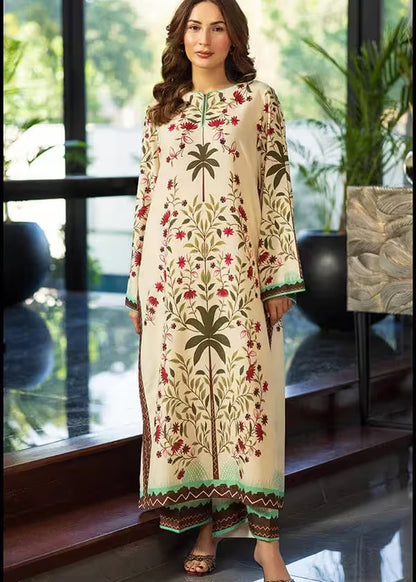 Woman wearing a long, floral embroidered dress standing indoors with plants in the background.