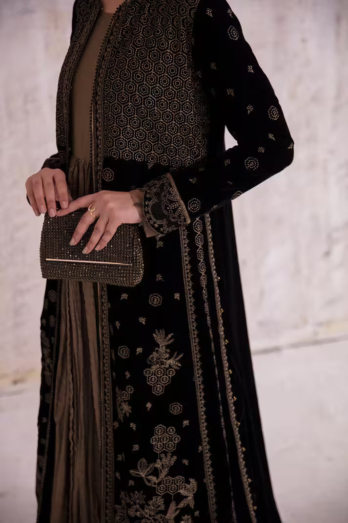 Person wearing a black embroidered outfit holding a matching clutch against a neutral background