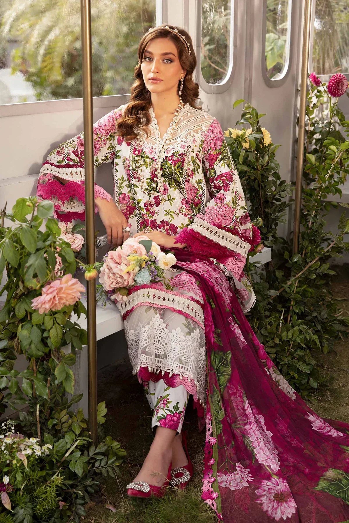 Woman in a floral and embroidered outfit sitting among flowers and greenery.