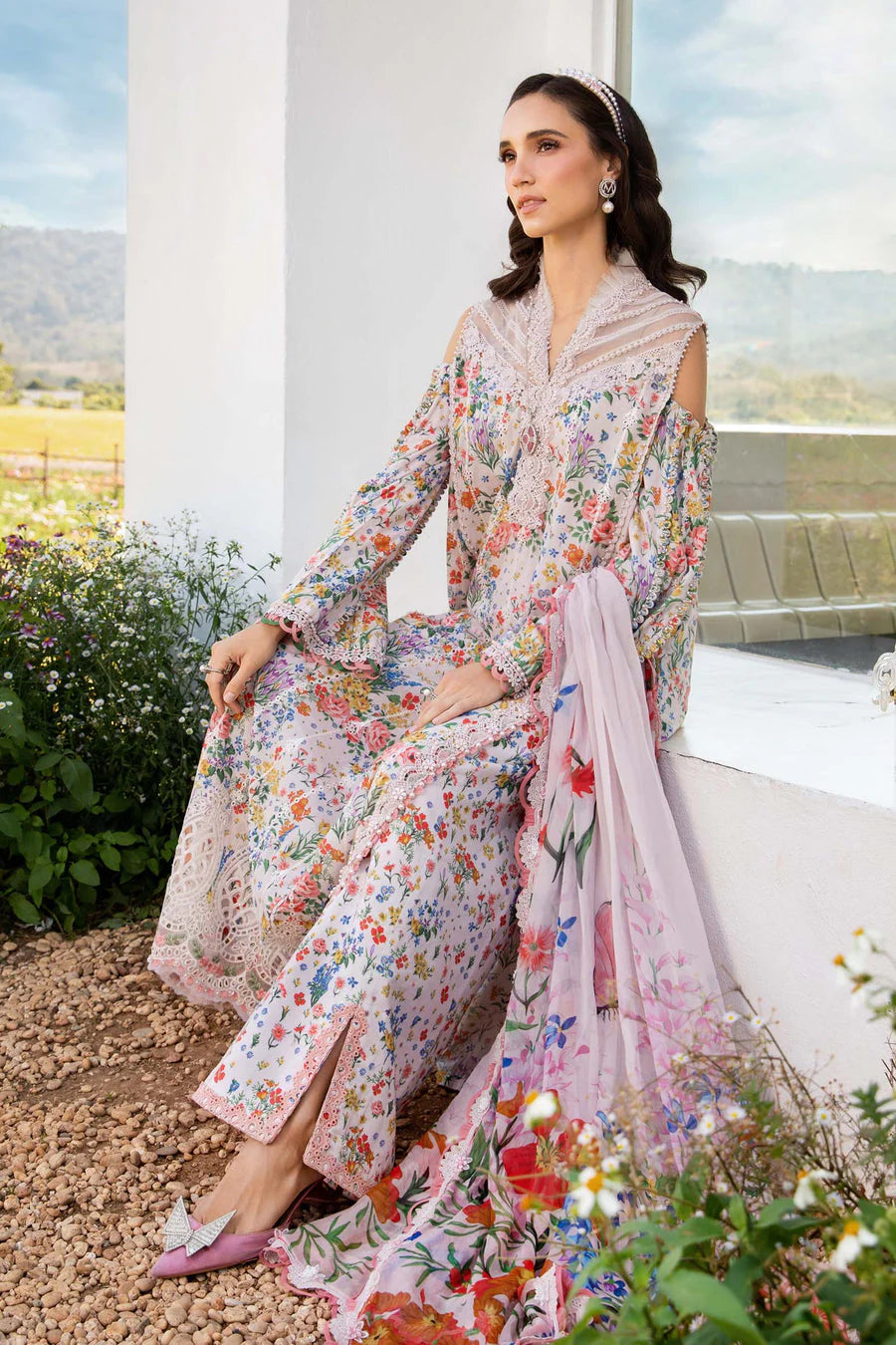 Woman in a floral dress and pink dupatta sitting outdoors with a scenic background
