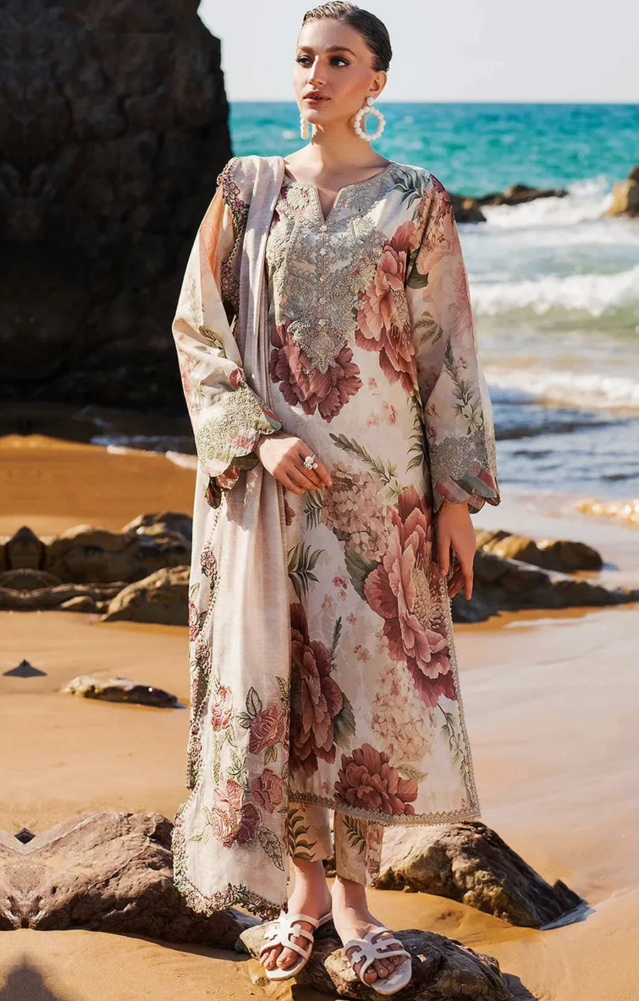 Woman in a floral dress standing on a beach with ocean in the background