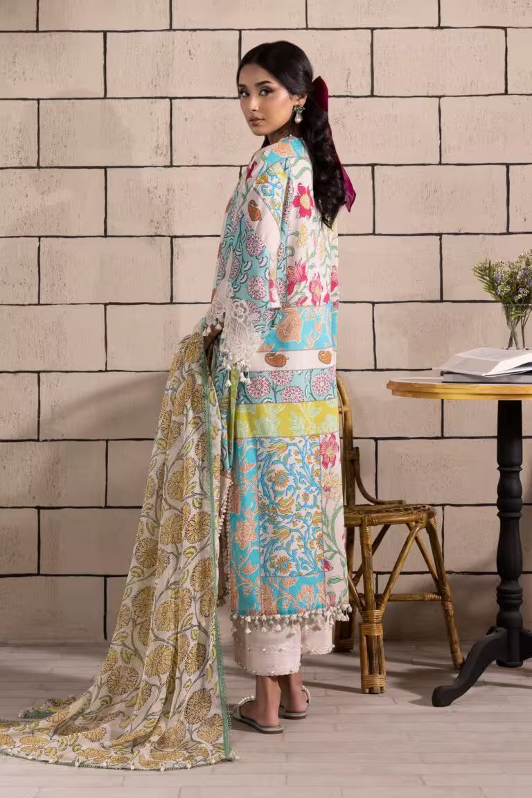 Woman in a colorful traditional outfit standing against a brick wall with a table and chair in the background.