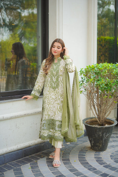 Woman in a green and white traditional outfit standing by a window with a plant in the foreground.